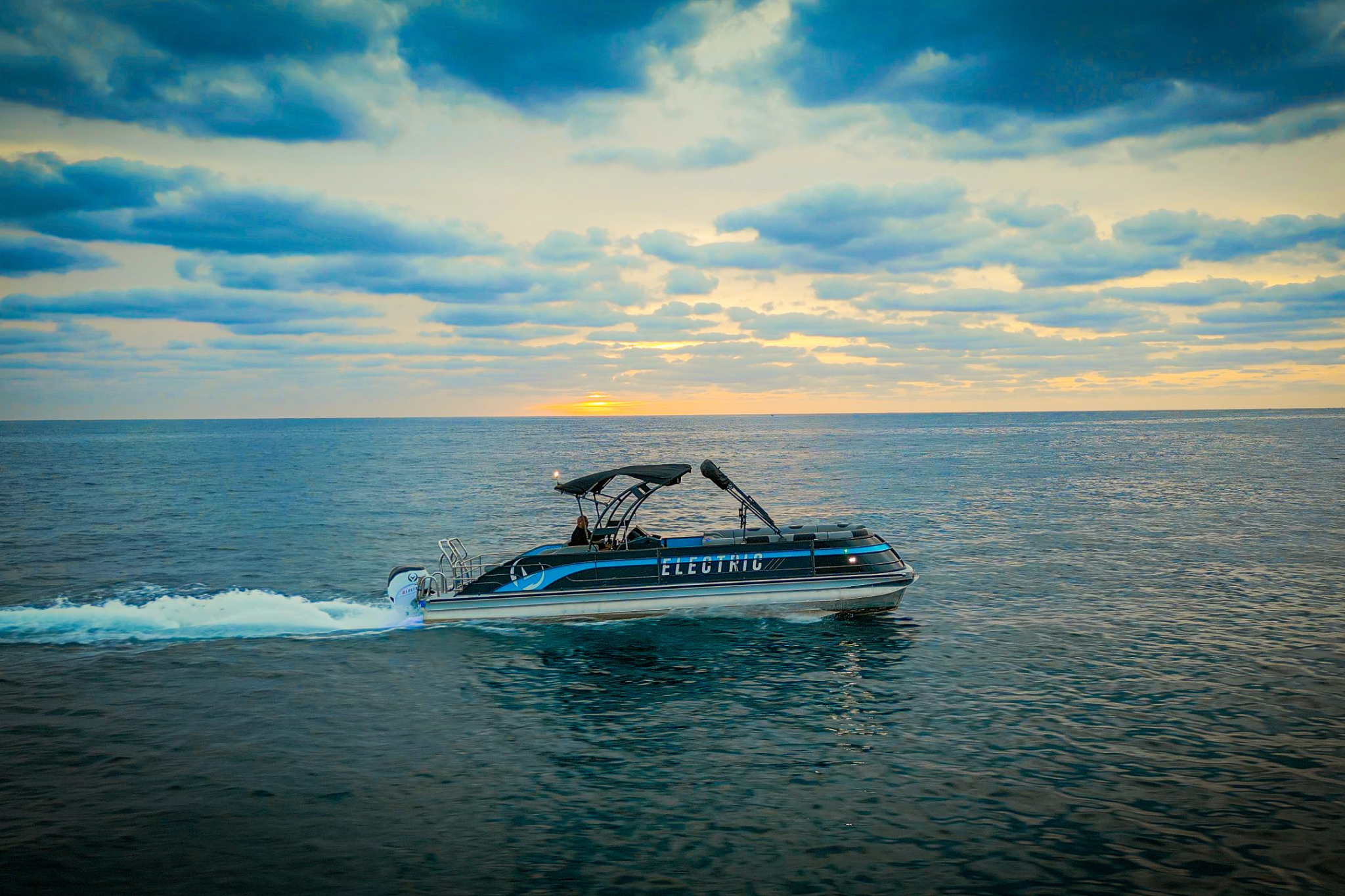 The V30 Electric Pontoon cruising on open water at sunset, showing its large footprint, stable tritoon platform, and suitability for spacious, all-day electric cruising.