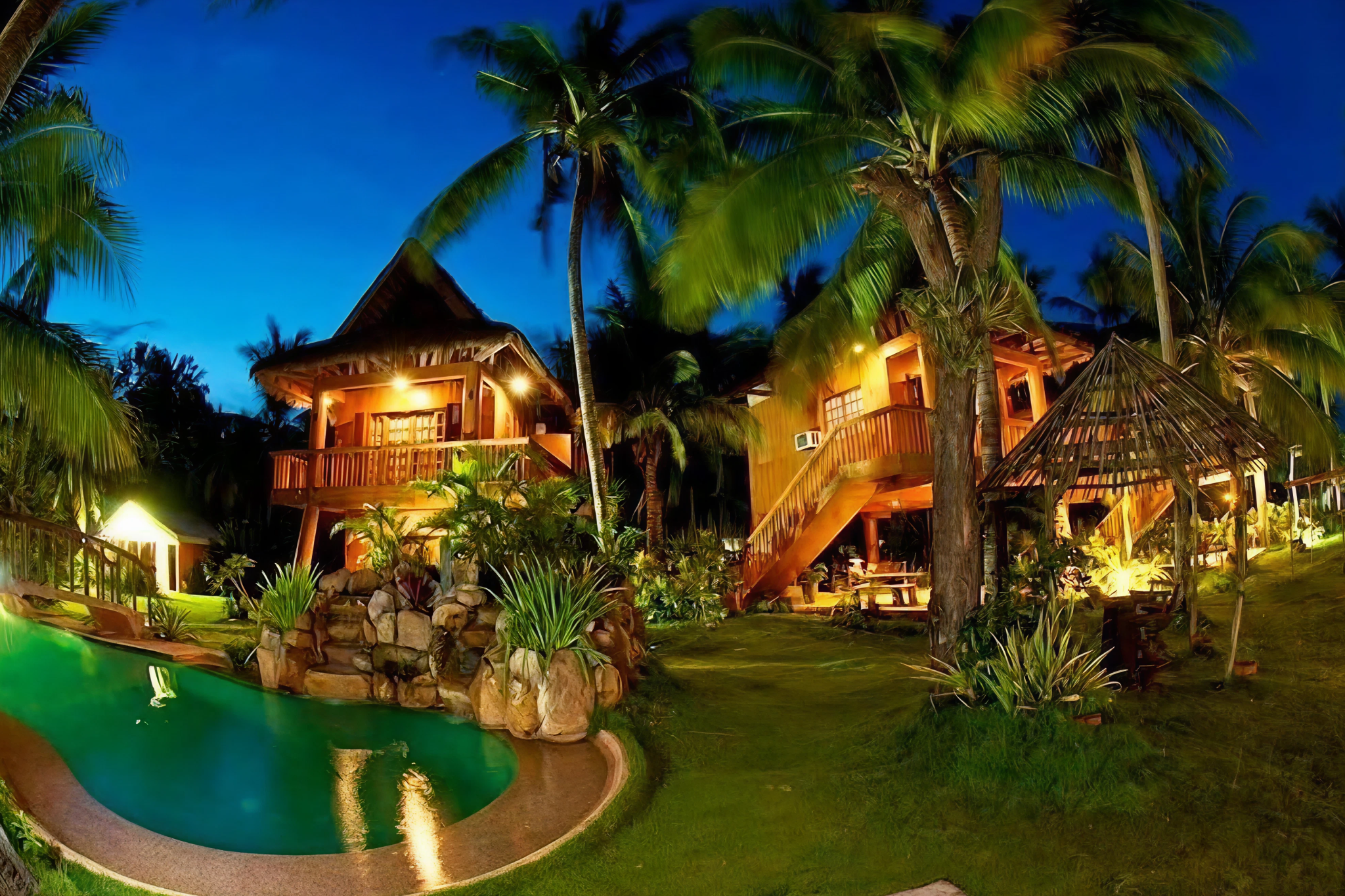 Tropical garden villas lit warmly at night with a lagoon-style pool and tall coconut trees at Hoyohoy Villas — Where to Stay in Bantayan Island.