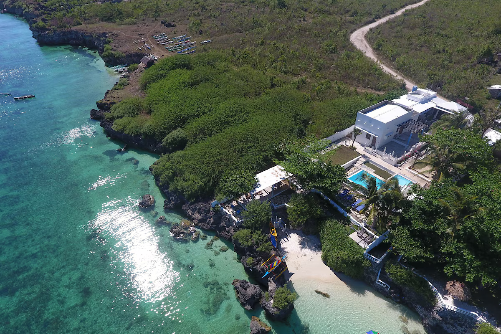 Aerial view of Kandugyap House by the Sea, a white cliffside villa overlooking crystal-clear blue waters and lush coastal greenery — Where to Stay in Bantayan Island.