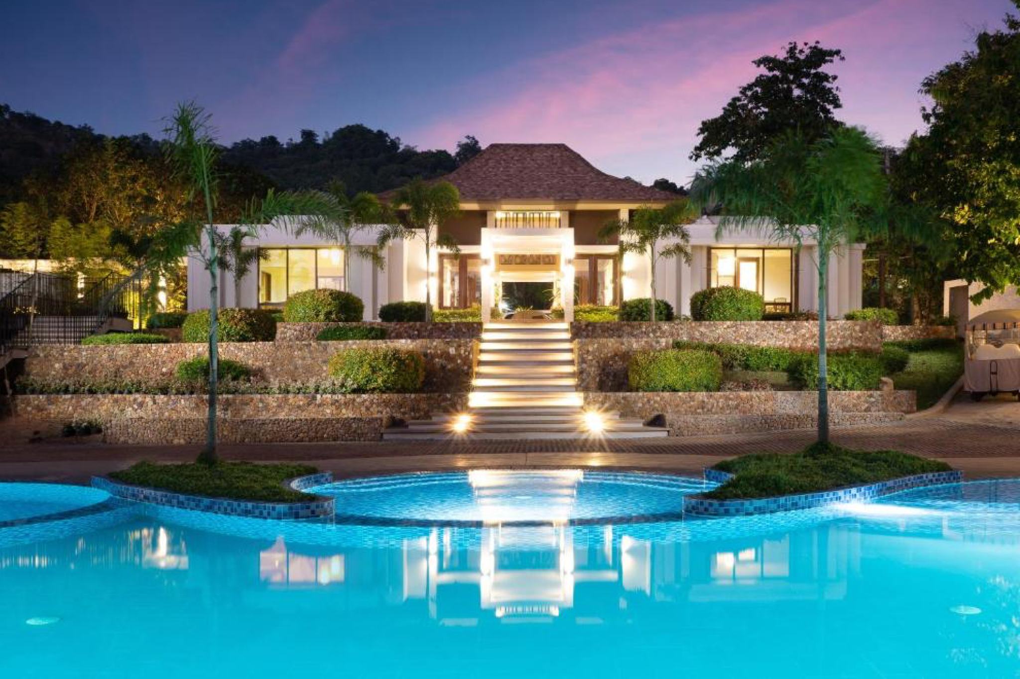 Illuminated entrance and tiered pool of Bacau Bay Resort Coron at dusk, blending contemporary comfort with tranquil surroundings — an inviting option for Where to Stay in Coron.