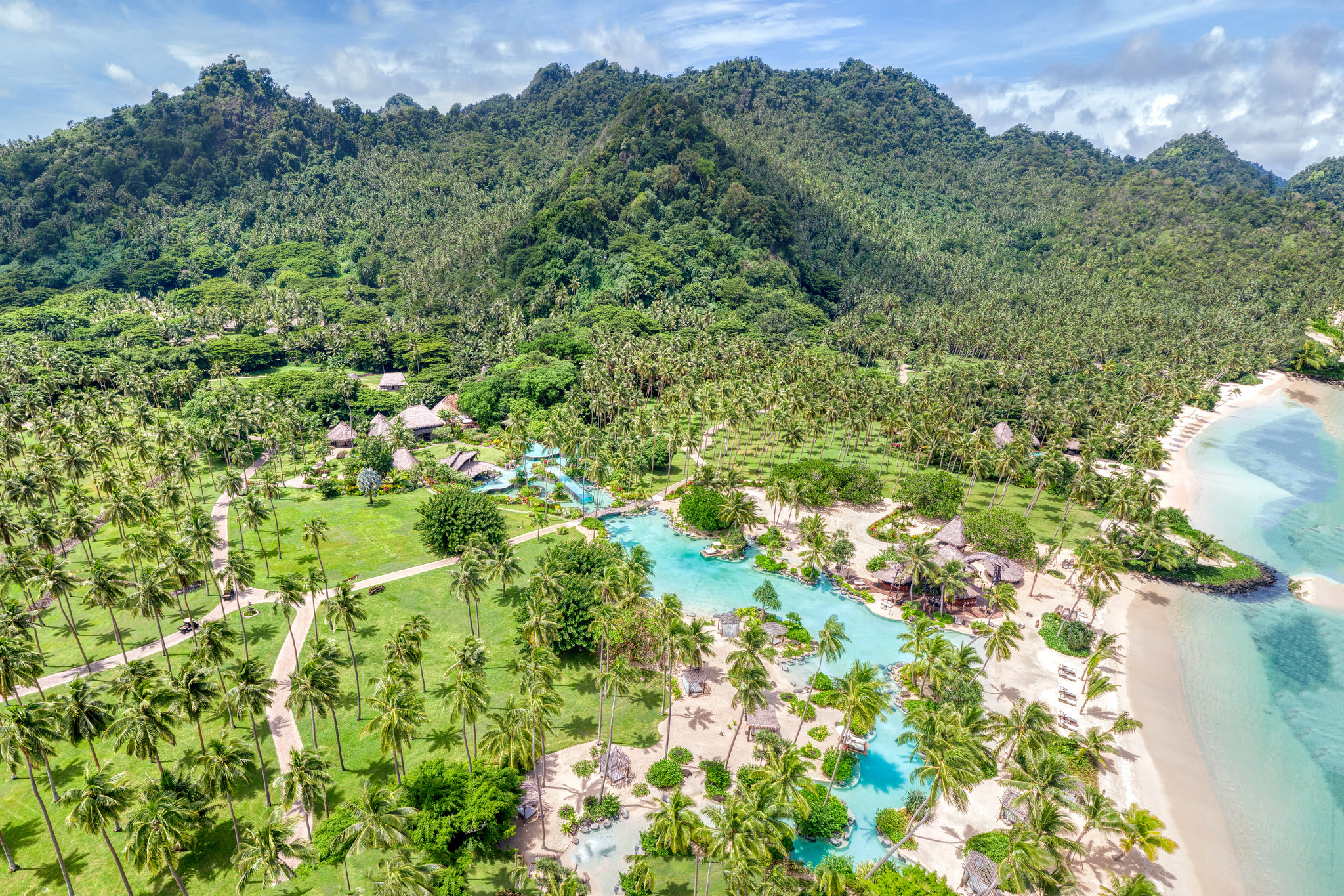 Aerial view of a lush, tropical island in Fiji with dense palm trees, white sandy beaches, and turquoise coral reefs, a private resort island among billionaire islands owned by Dietrich Mateschitz’s estate.