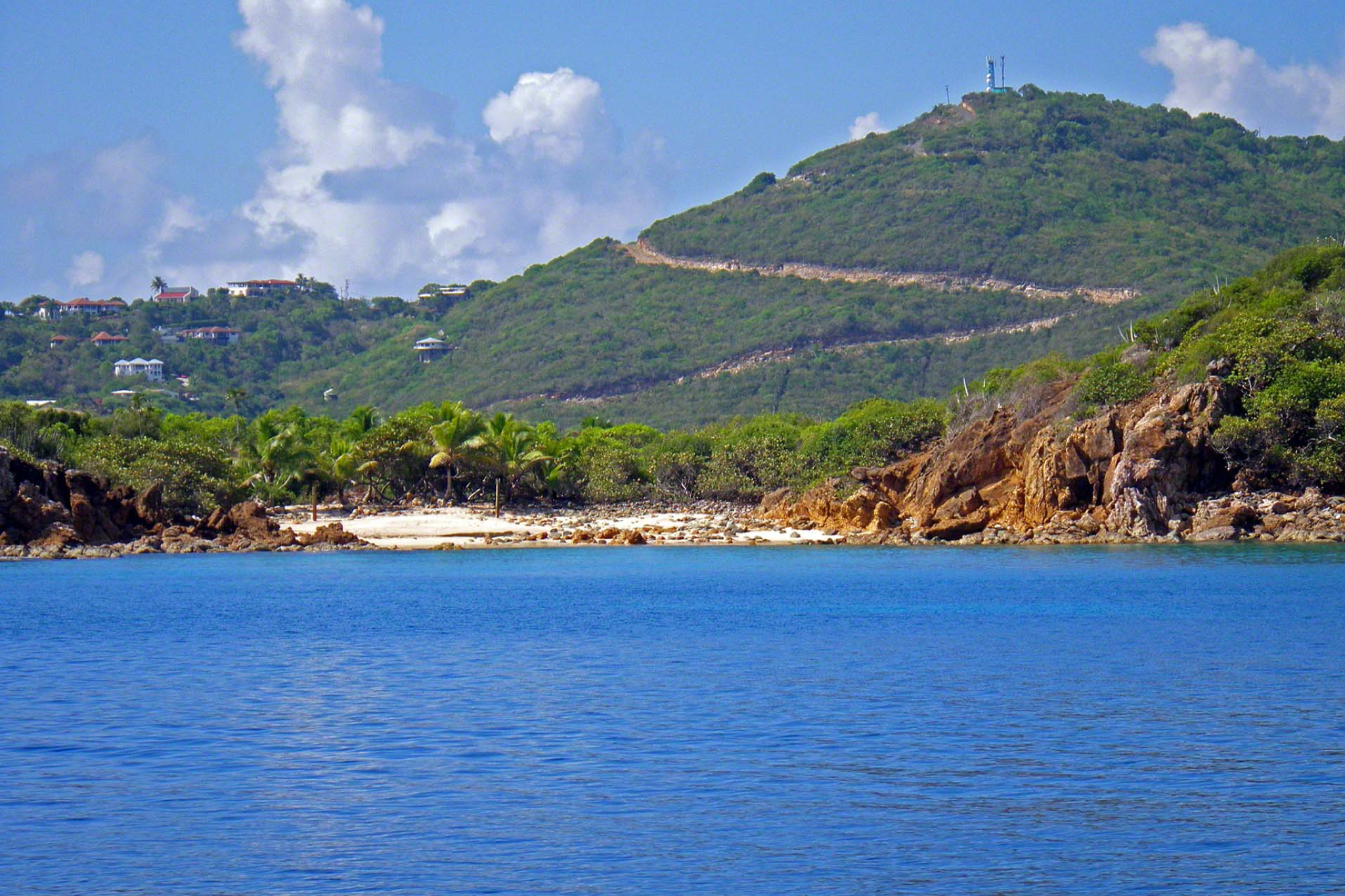 Dense tropical forest covering rocky coastline with clear shallow waters, part of the billionaire islands portfolio owned by Richard Branson in the British Virgin Islands.