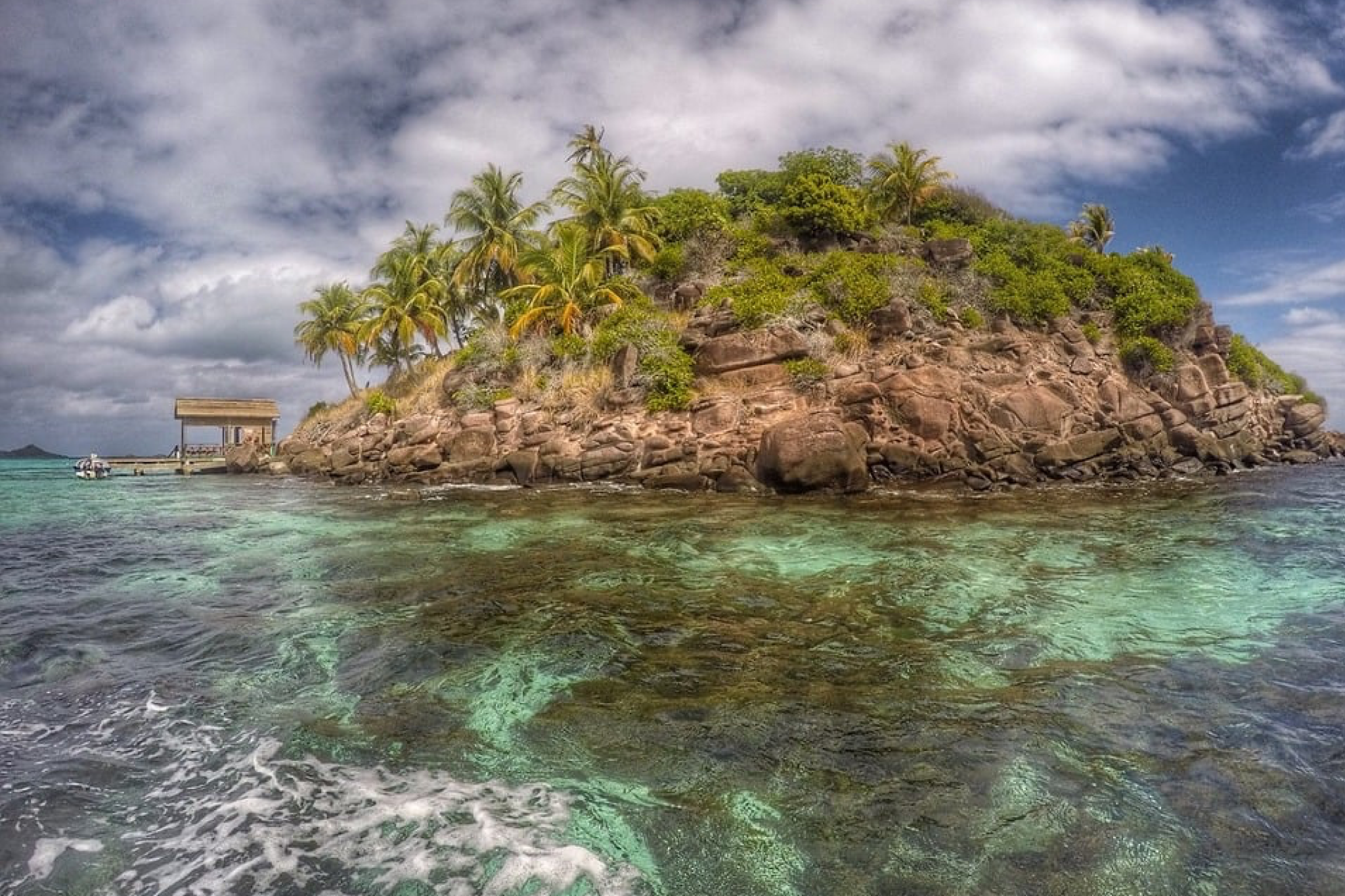 Turquoise waters surrounding a lush, small tropical island with palm trees and rocky shoreline, a private island in the Bahamas known among billionaire islands owned by David Copperfield.