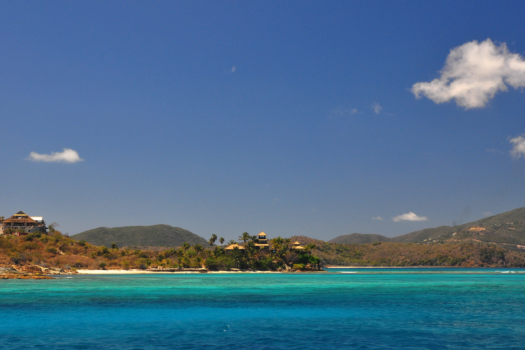 Small green island with sandy beaches and luxury villas, set against a bright blue sky and sea, a famous Caribbean billionaire island owned by Richard Branson.