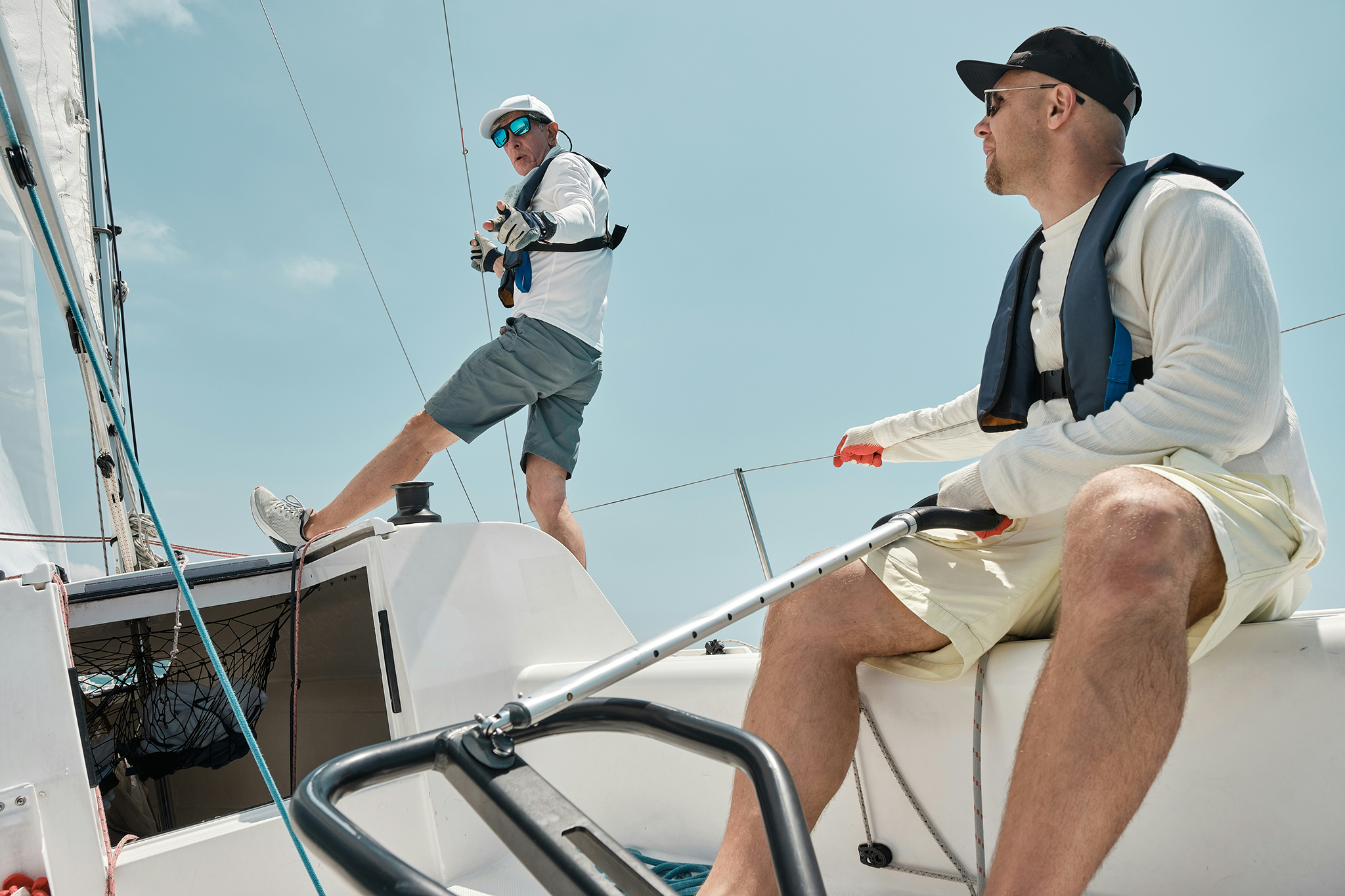 Yacht vs boat lifestyle comparison showing two men manually sailing a small boat, reflecting hands-on operation.